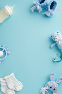Bebek oğlan konsepti. En üstteki dikey çizme fotoğrafı çoraplar, yumuşatıcı oyuncak oyuncak süt şişesi ve izole edilmiş pastel mavi arka planda örülmüş tavşan çıngırağı oyuncağı ortada boş alan.