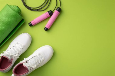 Spor aksesuarları konsepti. Beyaz spor ayakkabıları spor paspasının üst görünümü ve izole edilmiş yeşil arka planda ip atlama telif alanı