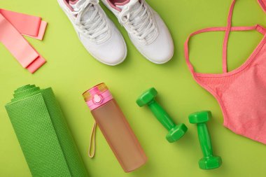 Spor aksesuarları konsepti. Pembe spor sutyen, spor ayakkabısı, su yeşil spor paspas bandı ve izole edilmiş yeşil arka planda dambıllar.