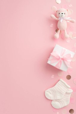 Bebek aksesuarları konsepti. Beyaz hediye kutusunun dikey resmi kurdeleli oyuncak ayıcığın minicik çorapları ve izole edilmiş pastel pembe arka planda parlak konfetileri.