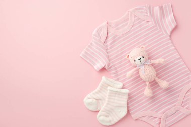 Bebek konsepti. Bebek kıyafetleri, pembe vücut giysisi çorapları ve izole edilmiş açık pembe arka planda oyuncak bebek oyuncakları.
