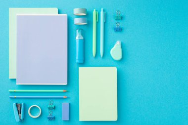 Okul konseptine geri dönelim. Sipariş edilmiş kırtasiye bileşiminin üst görünümü fotokopi kitapları yapıştırıcı bant klipsleri kalemler silgi zımbaları ve izole edilmiş mavi arkaplanda düzelticiler.