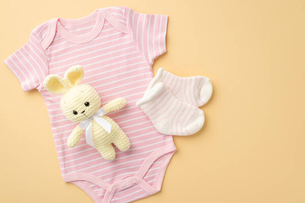 Концепция детских принадлежностей. Фотография сверху розового бодибилдера и вязаной игрушки кролика на изолированном бежевом фоне