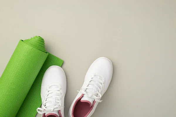 Fitness accessories concept. Top view photo of white sports footwear and green yoga mat on isolated pastel grey background with copyspace