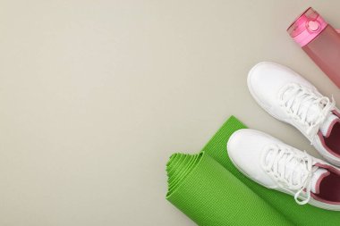 Aktif yaşam konsepti. Beyaz spor ayakkabıları, pembe su şişesi ve yeşil egzersiz paspası, izole edilmiş pastel gri arka plan ve kopyalanmış alan.