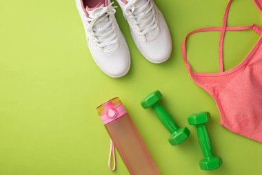 Fitness konsepti. Pembe spor sutyen, spor ayakkabısı, su şişesi ve yeşil halterlerin izole edilmiş yeşil arka plan fotoğrafı.
