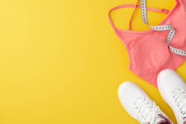 Spor konsepti. Pembe spor sutyen beyaz ayakkabılar ve izole edilmiş sarı arkaplan üzerindeki mezuranın üst görünümü