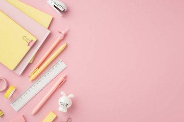 Okul konseptine geri dönelim. Okul aksesuarlarının, kalemlerin, cetvel mini zımba klasörlerinin, yapıştırıcı bant silgisinin ve izole edilmiş pembe arka planda tavşan şekilli bileyicinin en iyi görüntüsü.