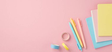 Okul konseptine geri dönelim. Üst panoramik manzara okul malzemelerinin dikey fotoğrafı renkli not defterleri kalemler ve izole edilmiş pembe arka planda yapıştırıcı bant.