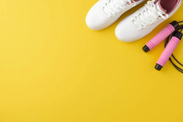 Sports accessories concept. Top view photo of pink skipping rope and white sneakers on isolated yellow background with empty space