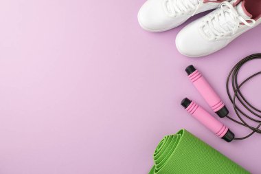 Spor aksesuarları konsepti. Üst görünümde pembe ip atlayan yeşil spor minderi ve beyaz spor ayakkabıları ile izole edilmiş pastel eflatun arka planda