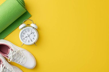 Fitness konsepti. Beyaz spor ayakkabılarının en üstteki fotoğrafı yeşil spor paspas ve izole edilmiş sarı arka plandaki alarmlı saat.