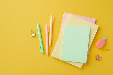 Okul malzemeleri konsepti. İzole edilmiş sarı arkaplanda ananas şekilli silgi klipleri ve kalemlerin renkli kırtasiye yığınının üst görünümü