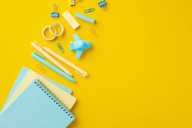 Okul konseptine geri dönelim. Okul aksesuarlarının, uçak şekilli bileme kitaplarının, cilt kliplerinin, yapıştırıcı bantların ve kopyalanmış sarı arka planda bulunan kalemlerin en iyi görüntüsü.