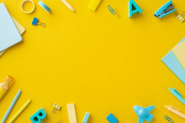 Okul konsepti. Not defterlerinin üst görünüm fotoğrafı plastik alfabe harfleri zımba yapıştırıcı bant silgileri düzeltici düzlem biçimli kalemler izole edilmiş sarı arka plan ortada boş alan