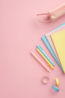 Okul konseptine geri dönelim. Okul malzemelerinin dikey üst görüntüsü renkli not defterleri kalem kutusu ve izole edilmiş pembe arka planda yapıştırıcı bant.