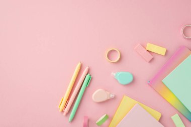 Okul malzemeleri konsepti. Renkli kırtasiye defterlerinin en üst görünüm fotoğrafı. Düzeltme silgisini yuvarlak kalemler ve izole edilmiş pembe arkaplandaki yapışkan bantlar.