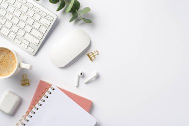 Business concept. Top view photo of workstation keyboard computer mouse eucalyptus cup of hot drinking wireless earbuds gold binder clips and pink notebooks on isolated white background