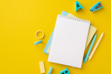 School accessories concept. Top view photo of stationery notepads plastic alphabet letters mini stapler adhesive tape erasers and pens on isolated yellow background with blank space