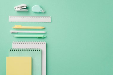 Okul konseptine geri dönelim. Okul gereçlerinin en üst görüntüsü not defterleri. Düzeltme bant cetveli ve tel zımba, izole edilmiş pastel yeşil arka planda.