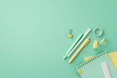 School supplies concept. Top view photo of stationery notepads pens ruler binder clips and adhesive tape on isolated pastel green background with empty space