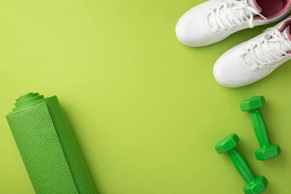 Sports accessories concept. Top view photo of white footwear green exercise mat and dumbbells on isolated green background with copyspace