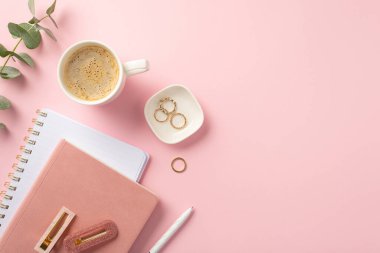 Business concept. Top view photo of workspace pink planners pen stylish hairpins gold rings cup of coffee and eucalyptus on isolated pink background with copyspace