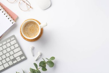 İş konsepti. Rattan placemat kablosuz kulaklıklar üzerinde işyeri kahve fincanının üst görüntüsü fare klavye bilgisayarı fotokopi kitapları gözlüğü ve izole edilmiş beyaz arka planda okaliptüs.