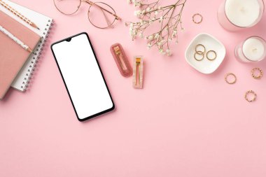 İş konsepti. İş yerindeki akıllı telefon mumlarının üst görüntüsü günlükler şık gözlükler altın yüzükler ve izole edilmiş pastel arka planda beyaz çigila çiçekleri.
