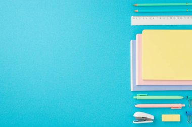 Okul konseptine geri dönelim. Düzenli kompozisyon kırtasiye yığını mini zımba kalemleri silgi klasör klipleri ve kopyalanmış mavi arkaplan üzerindeki kalemlerin üst görünümü