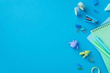 Okul konseptine geri dönelim. Kırtasiye hayvanı şekilli silginin üst görünüm fotoğrafı yapıştırıcı bant mini zımba bağlayıcı raptiyeler kalemler ve kopyalanmış mavi arkaplan üzerine not defterleri