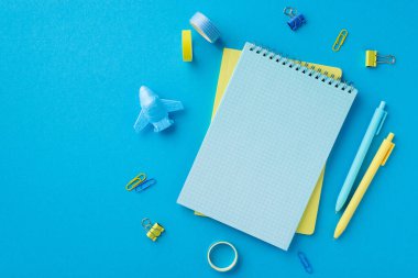 Back to school concept. Top view photo of school supplies notebooks pens adhesive tape plane shaped sharpener and binder clips on isolated blue background with empty space