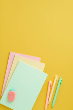 Okul konseptine geri dönelim. Renkli okul malzemelerinin dikey resmi ananas şekilli silgi yığını ve kopyalanmış sarı arka planda kalemler.