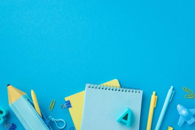 Okul aksesuarları konsepti. Kırtasiye defterlerinin en üstteki görüntüsü kalem, plastik alfabe harfleri uçak şekilli klasör klipleri ve izole edilmiş mavi arkaplan üzerindeki kalem kılıfı.