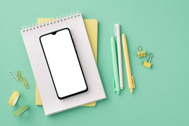 Back to school concept. Top view photo of school supplies smartphone on notepad pens binder clips and adhesive tape on isolated pastel green background with copyspace