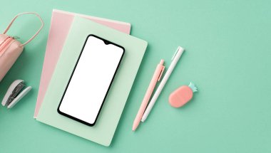 Back to school concept. Top view photo of mobile phone over copybooks pens pencil-case stapler and pineapple shaped eraser on isolated pastel green background with copyspace