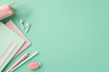 Okul konseptine geri dönelim. Okul malzemelerinin en üst görüntüsü not defterleri cetvel, kalem, ananas şekilli silgi ve izole edilmiş pastel yeşil arka planda boş alan ile kulaklık.