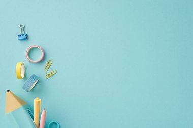 Okul konseptine geri dönelim. Renkli kırtasiye mavi kalem çantasının en üst görünümü. Kalem yapıştırıcı bant ve kopyalanmış pastel mavi arkaplan üzerindeki klasör klipleri.