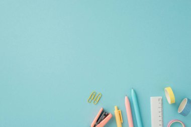 Okul konseptine geri dönelim. Renkli okul aksesuarlarının üst görünümü cetvel yapışkan bant ataçları ve izole edilmiş pastel mavi arka planda zımba.