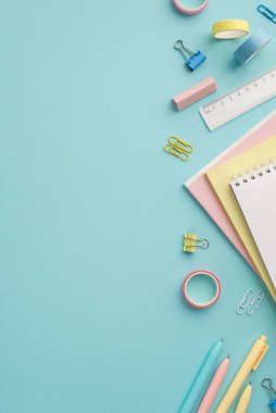 Back to school concept. Top view vertical photo of colorful stationery notepads eraser ruler adhesive tape pens and binder clips on isolated pastel blue background