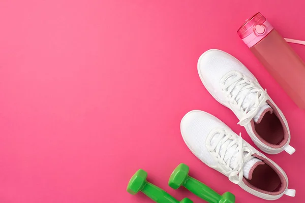 Sports concept. Top view photo of pink bottle of water green dumbbells and white shoes on isolated pink background with copyspace