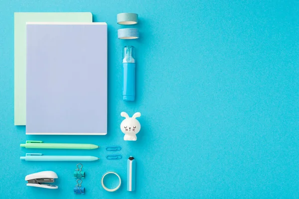 School accessories concept. Top view photo of ordered stationery notebooks adhesive tape binder clips pens eraser stapler correction pen bunny shaped sharpener isolated blue background with copyspace