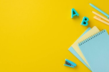 Okul konseptine geri dönelim. Okul aksesuarları, plastik alfabe harfleri, zımba zımbaları ve kalemlerin izole edilmiş sarı arka planda çekilmiş fotoğrafları.