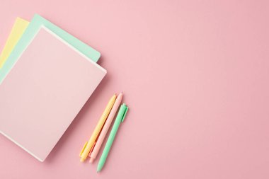 Okul konseptine geri dönelim. Okul malzemelerinin en üst görüntüsü renkli defterler ve kopyalanmış pembe arka plan üzerindeki kalemler