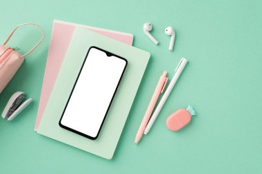 Back to school concept. Top view photo of smartphone over notebooks earbuds pens pencil-case mini stapler and pineapple shaped eraser on isolated pastel green background with empty space
