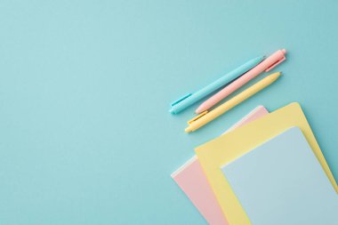 Okul malzemeleri konsepti. İzole edilmiş pastel mavi arkaplan üzerindeki renkli kırtasiye kalemlerinin ve kopya kitaplarının en üstteki görünümü