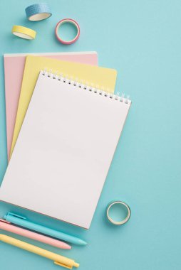 School supplies concept. Top view vertical photo of colorful school accessories stack of planners pens and adhesive tape on isolated pastel blue background with empty space