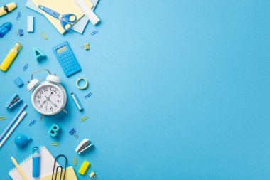 Okul konsepti. Alarm saatinin üst görünümü plastik alfabe harfleri düzeltme kalem zımbası zımba zımbırtısı silme not defteri yapışkan bant hesap makinesi makas cetvel kopyalanmış mavi arkaplan