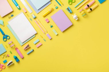 Top view photo of colorful school supplies copybooks pencils correctors marker pens binder clips staplers ruler adhesive tape scissors sharpeners erasers on isolated yellow background with copyspace