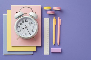 Okul konseptine geri dönelim. Okul malzemelerinin en üstteki fotoğrafı alarm saatini renkli kalemler silgi ve izole edilmiş menekşe arkaplanı üzerine yapıştırıcı bant.